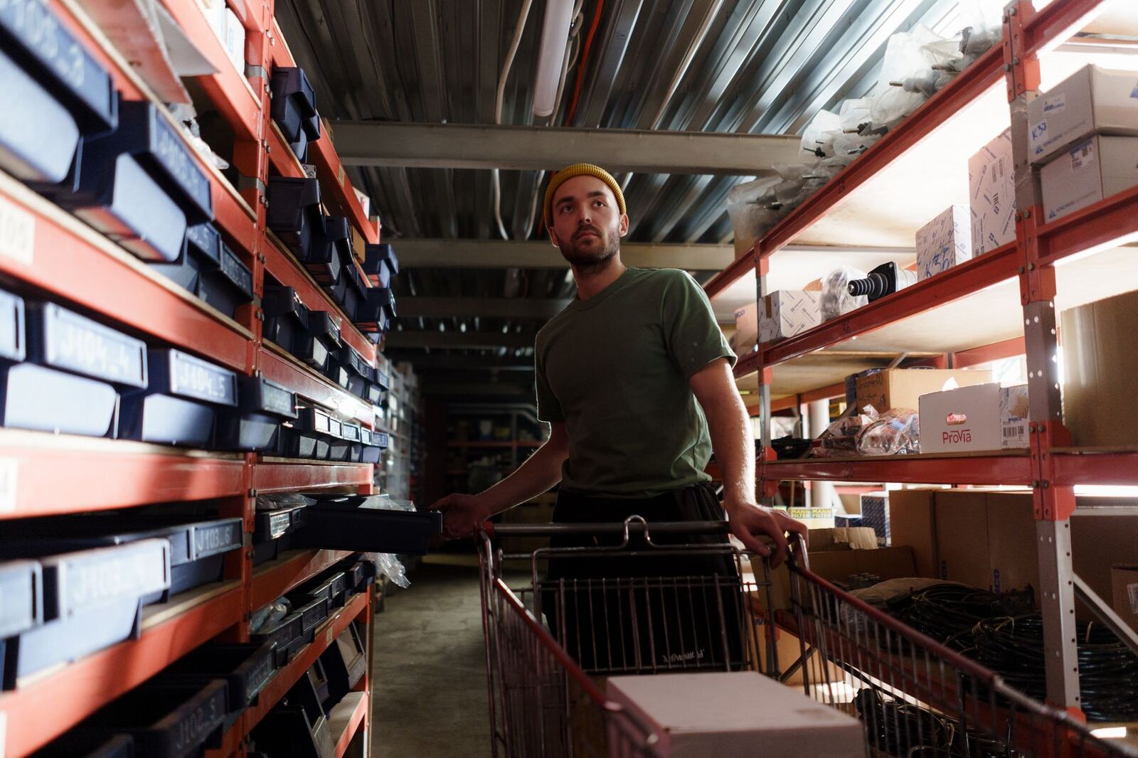 A warehouse worker organizing shelves with industrial products under the warehouse light.