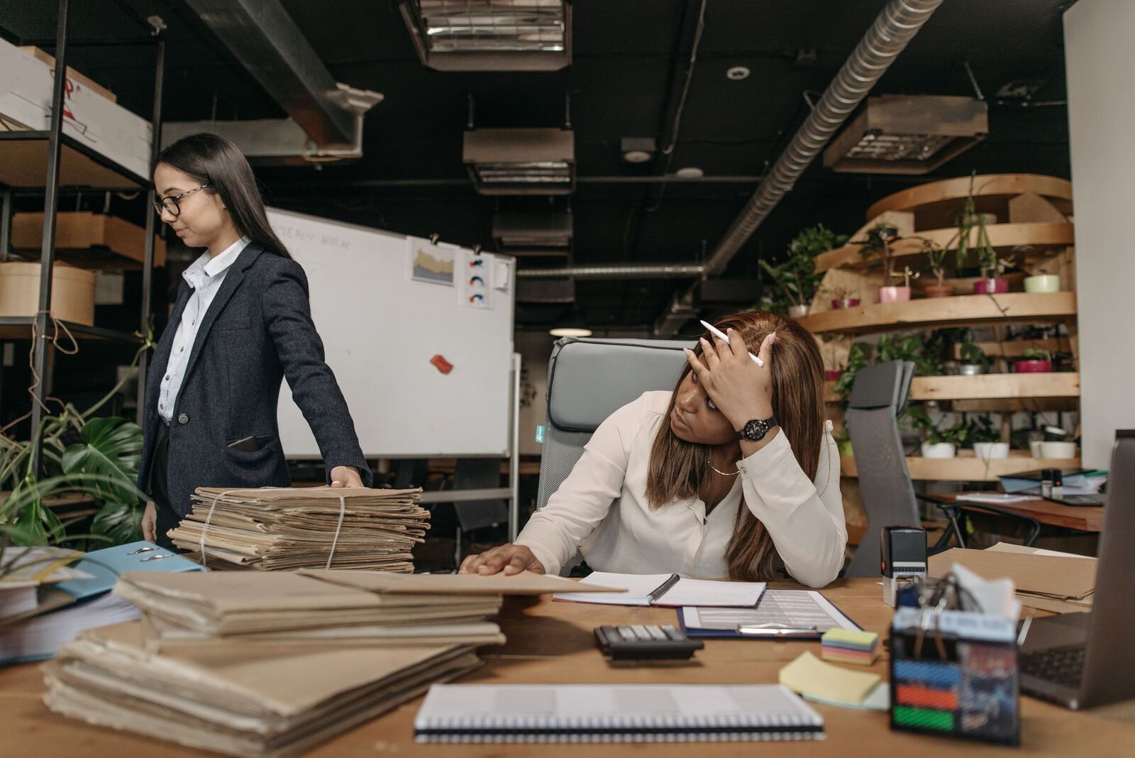 Two women working with documents in a modern office setting, one sitting at the desk, the other standing.