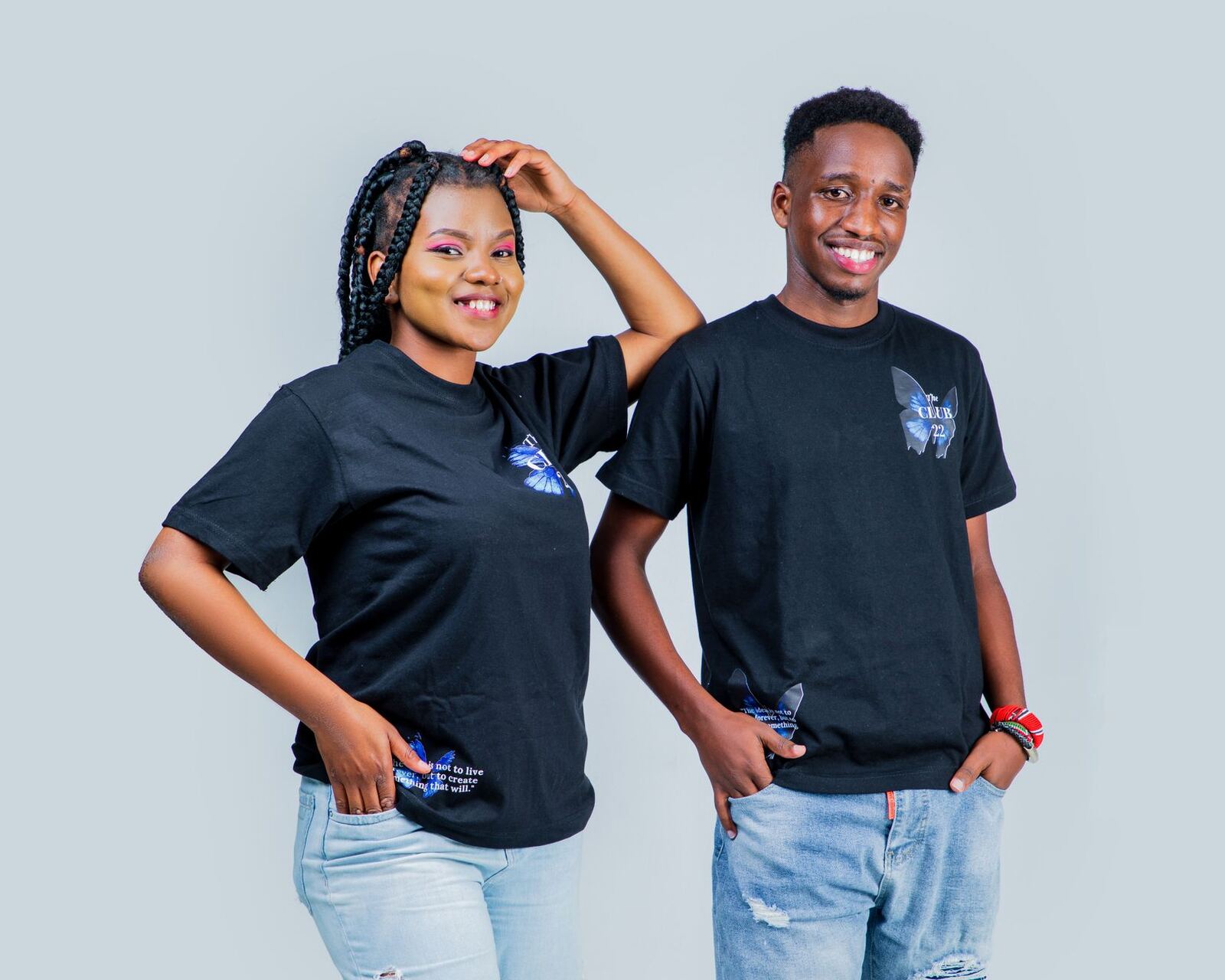 Smiling couple posing in black t-shirts and jeans during a studio photoshoot on a white background.