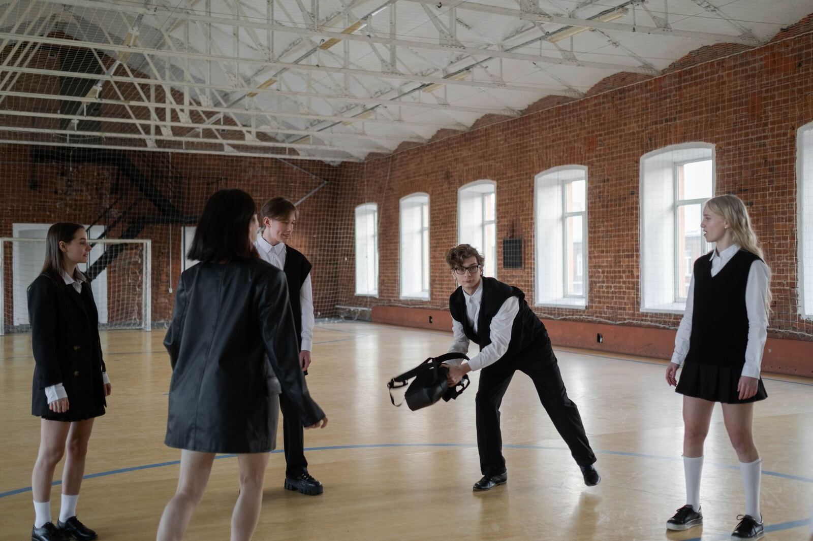 Teenagers in school uniforms interacting inside a brick-walled gymnasium, exploring social dynamics.