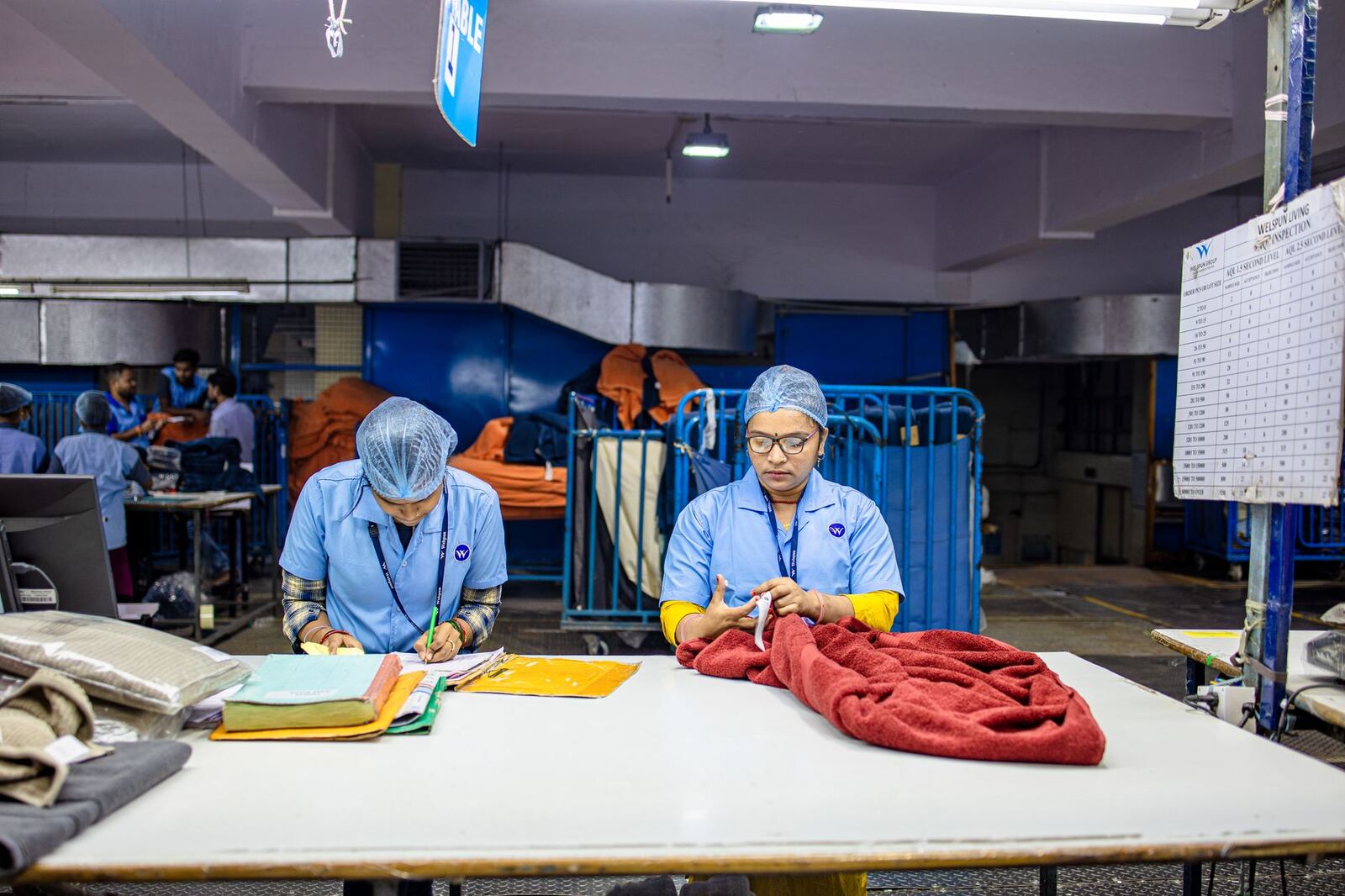 Two workers in a textile factory sorting fabric at a table under bright lighting.